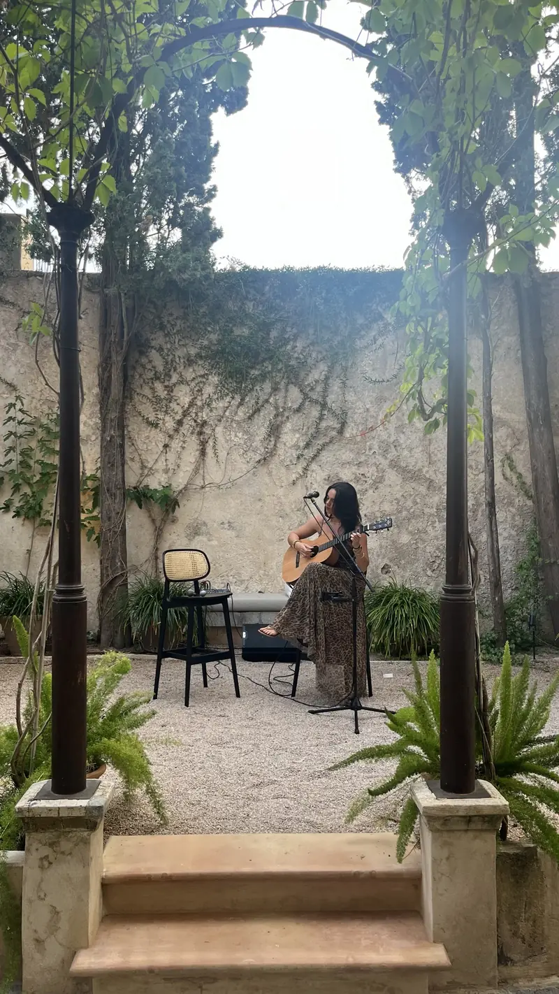 Llucia cantando con la guitarra en un patio con vegetación